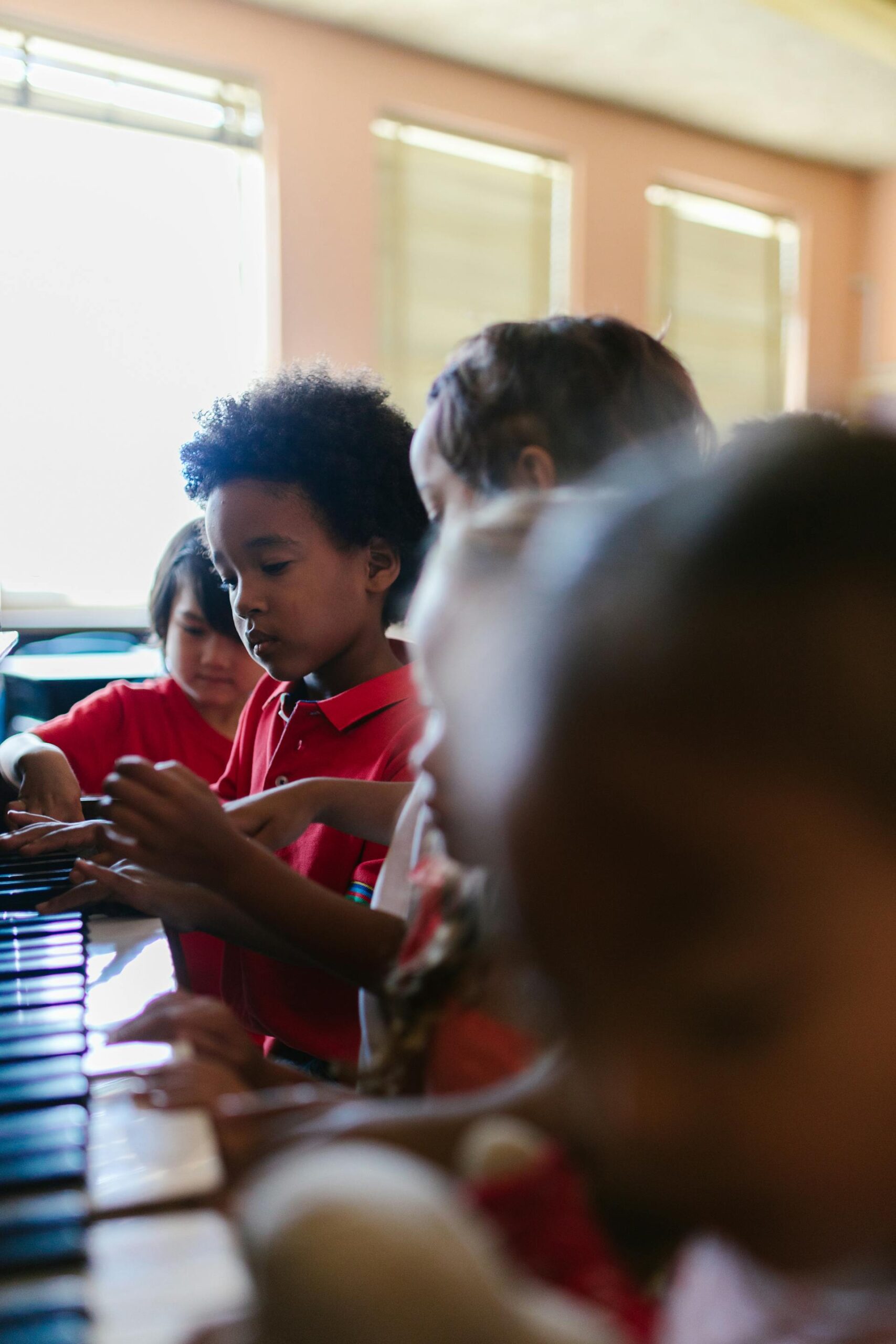 Children in a classroom setting gathered around a piano, focused and playing together, enjoying the creative experience of an Education Summer Camp in Singapore.